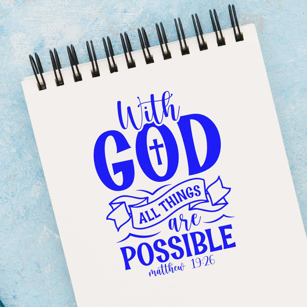 Blue rubber stamp and seal design on white spiral notebook, reading With God all things are possible Matthew 19:26.