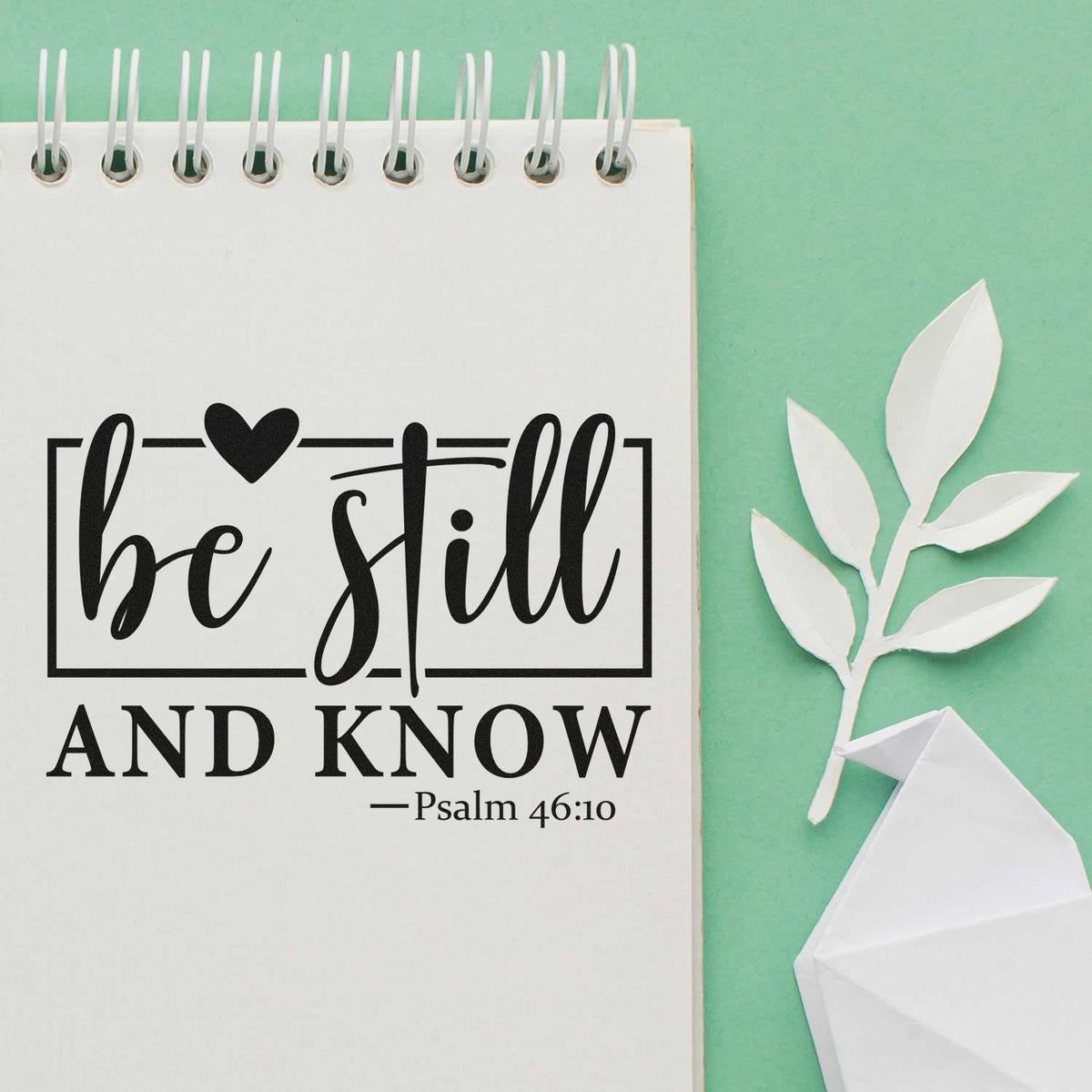 Black be still and know Psalm 46:10 stamp and seal on white notepad, with white paper leaf and origami dove on mint green.