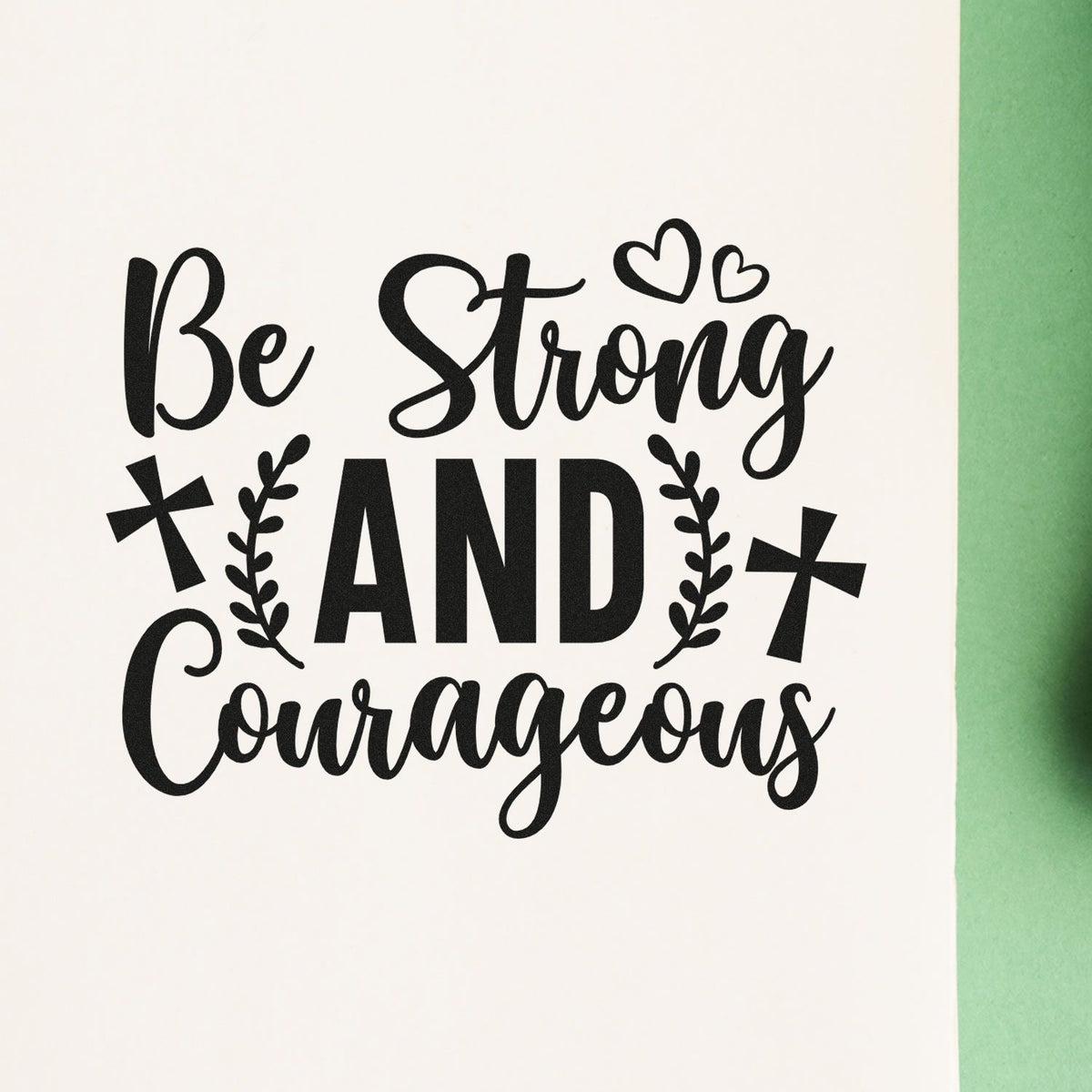 Black stamp and seal design reading Be Strong and Courageous with hearts, crosses, and leafy accents on white paper