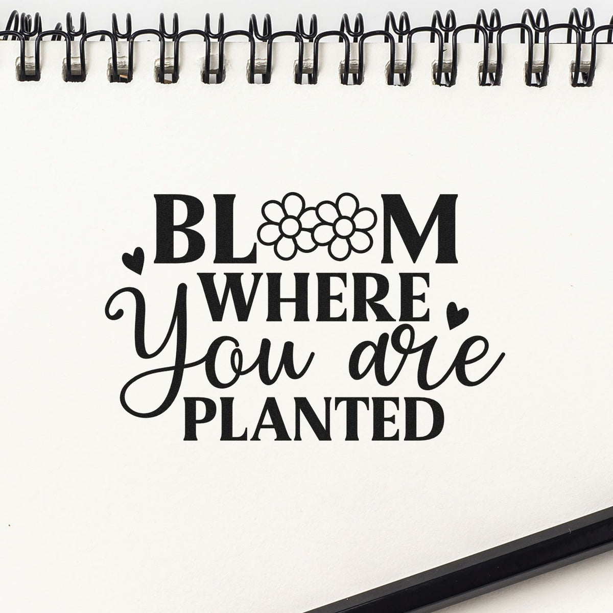 Black floral stamp and seal design on white spiral notebook: Bloom where you are planted with hearts.