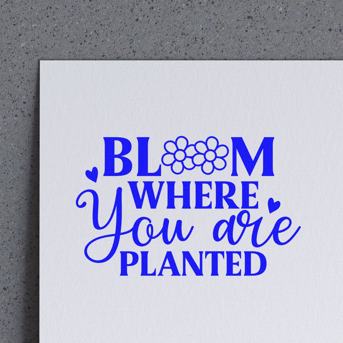 Blue stamp design on white paper reading Bloom where you are planted with flower icons and heart accents.