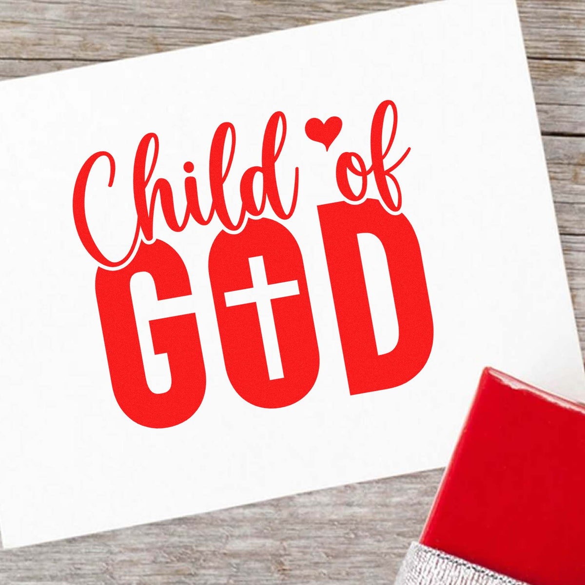 Red Child of God stamp design on white card with heart, beside a red seal block on a wood tabletop.
