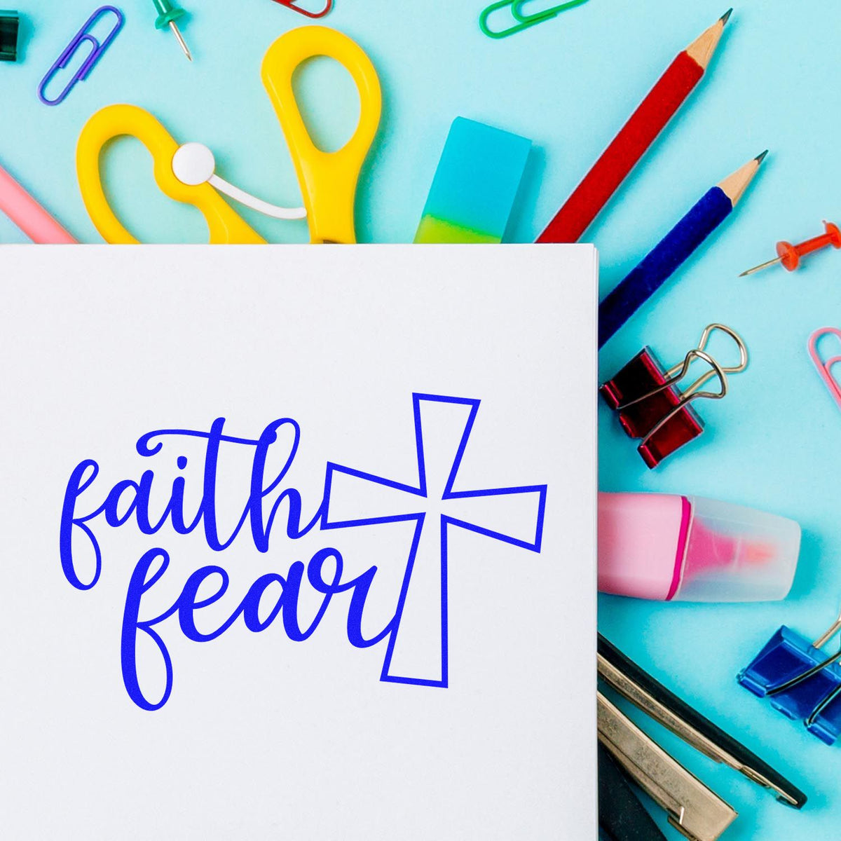 Faith over fear stamp and seal design in blue on white card, surrounded by colorful office supplies on an aqua background.
