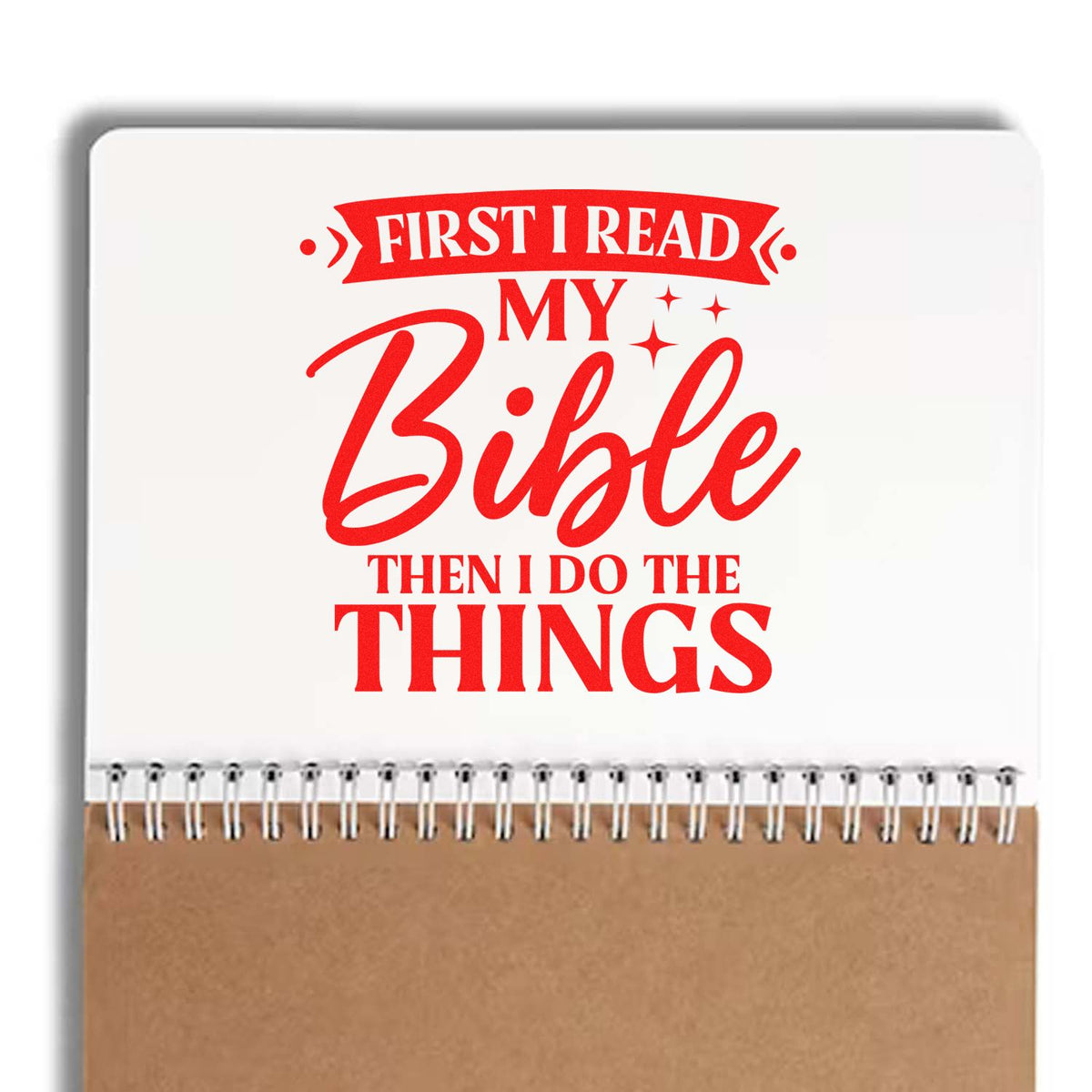 Red Bible stamp-style design on white spiral notebook with brown bottom, reading First I read my Bible then I do the things.
