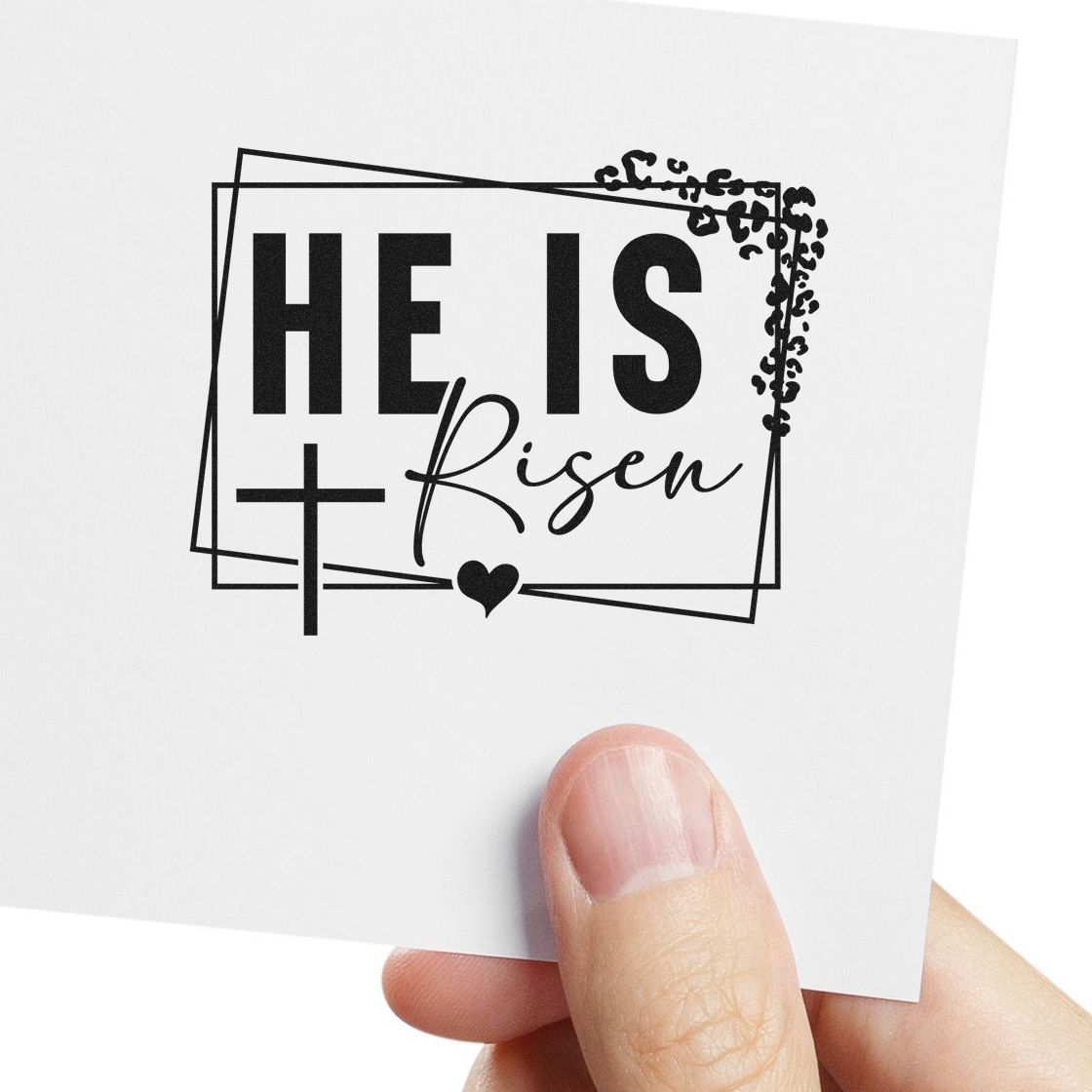 Black HE IS Risen stamp and seal design with cross, heart, and ornate border on white card.
