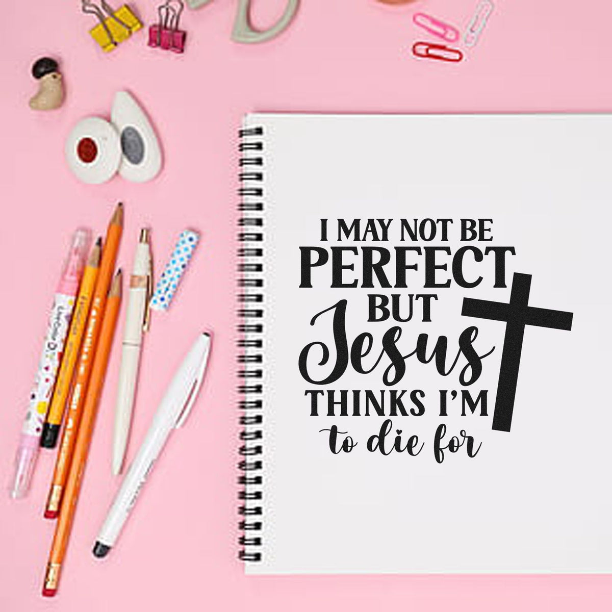Pink flat lay with spiral notebook, pens, binder clips, and stamp/seal supplies beside a faith quote on the cover.