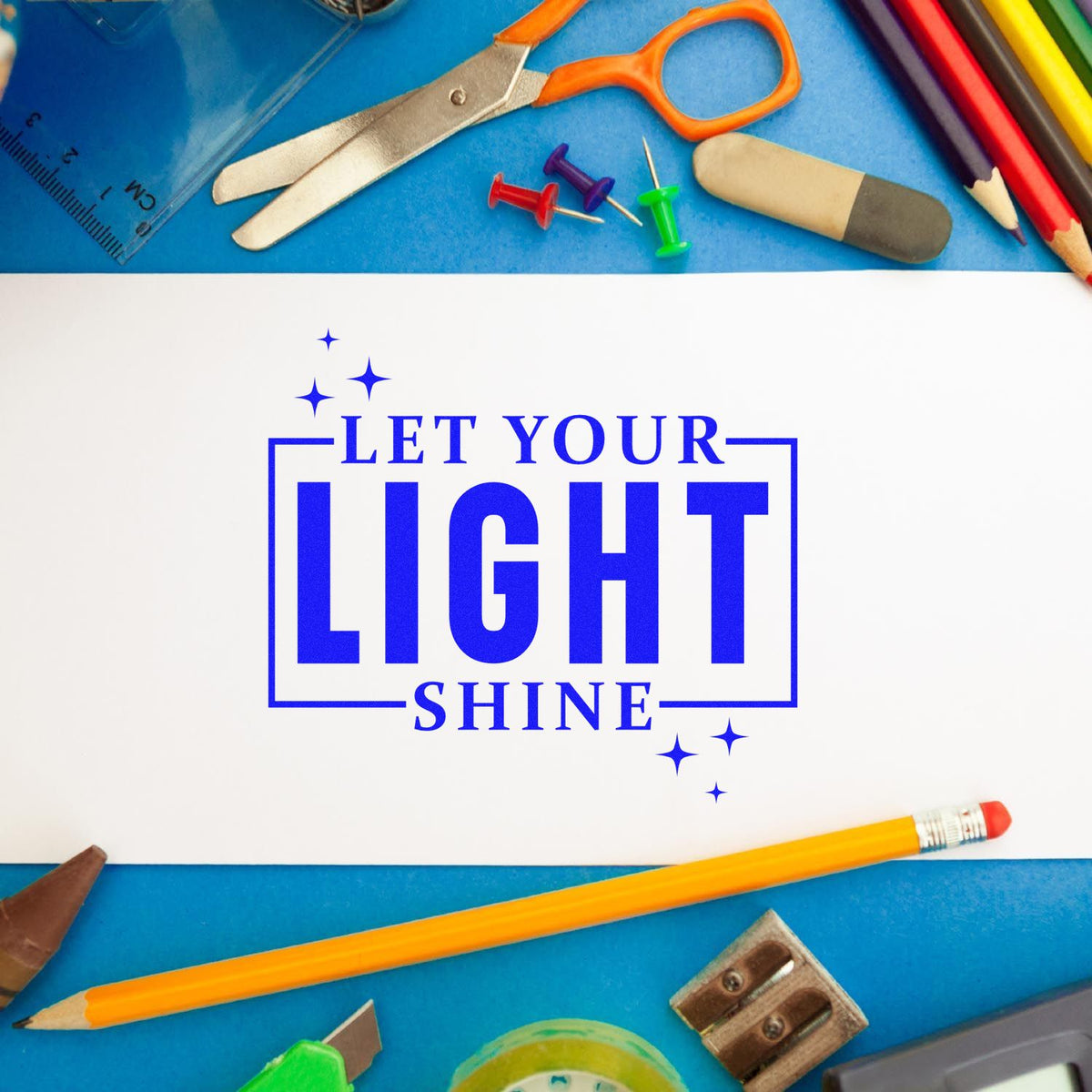 Blue stamp and seal design reading Let Your Light Shine, surrounded by colorful school supplies, scissors, pencils, and pushpins.