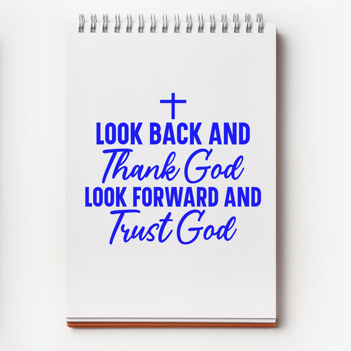 Blue religious stamp and seal on a white spiral notebook, with a cross and the words Look back and thank God, look forward and trust God.