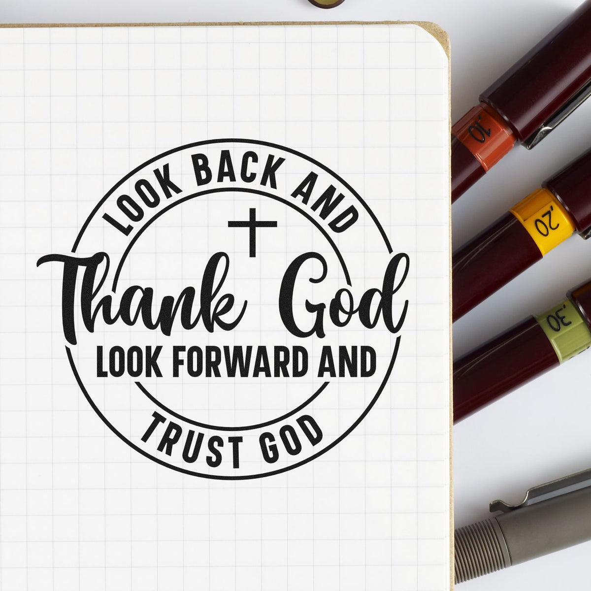 Black faith stamp seal on white grid notebook, with maroon, orange, yellow, green, and gray marker stamps.
