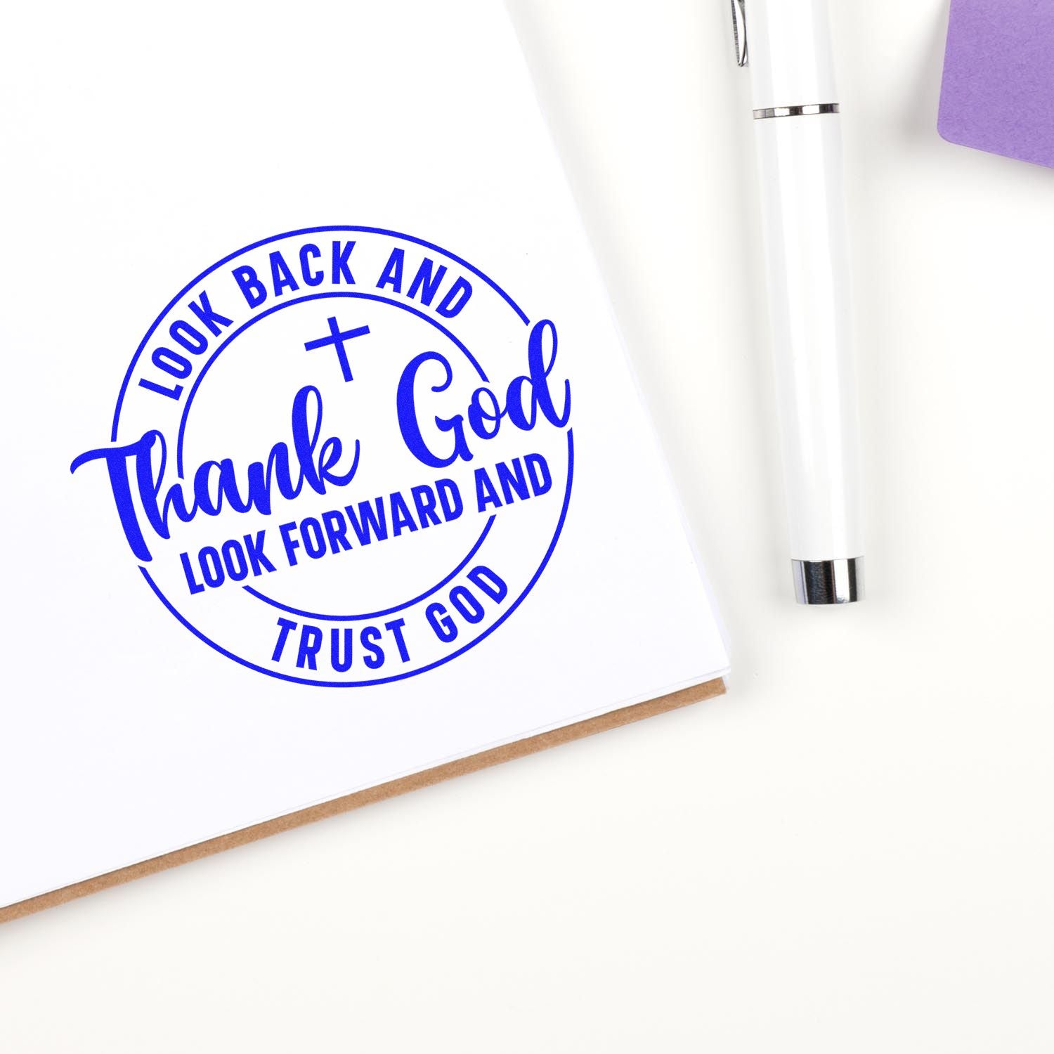 Blue circular stamp seal reading Thank God and Look back, look forward, trust God on white paper, beside a white pen.