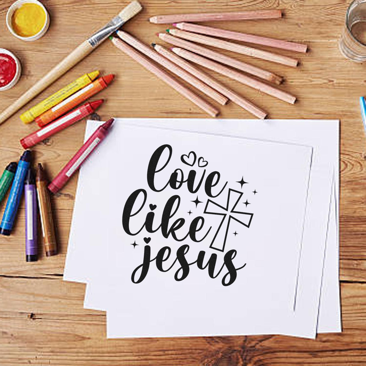 Black Christian stamp and seal design reading love like Jesus on white paper, with cross, hearts, and colorful pencils.