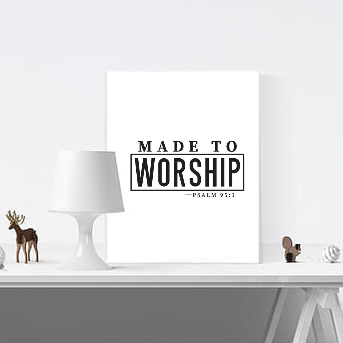 Black stamp-style seal reading Made to Worship Psalm 95:1 on white canvas, with a white lamp and small decor.