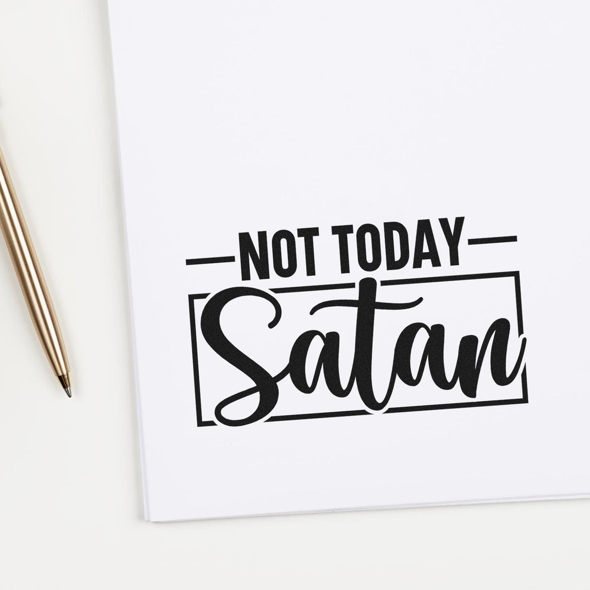 Black stamp/seal design reading Not Today Satan on white paper, with a gold pen beside it.