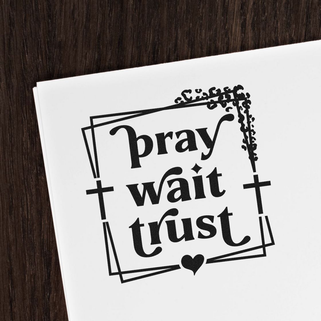 Black prayer stamp and seal reading pray wait trust with ornate frame, crosses, and heart on white paper.
