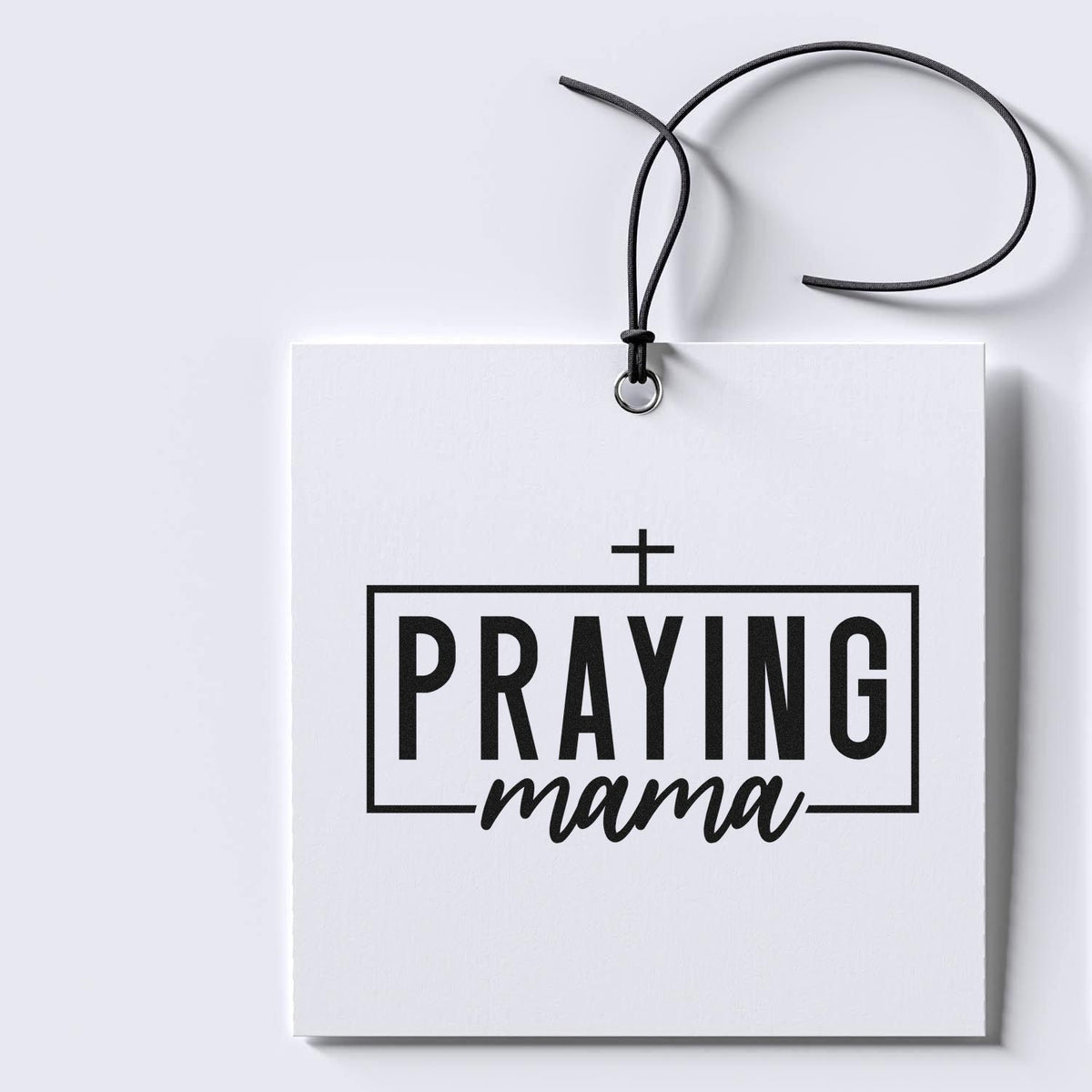 White stamp and seal hanging tag with black cord, cross, and bold black PRAYING mama text.