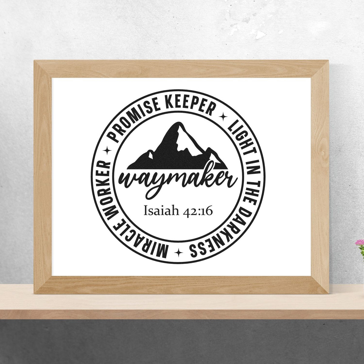 Black Christian stamp seal design with mountain, Waymaker text, Isaiah 42:16, in a light wood frame.