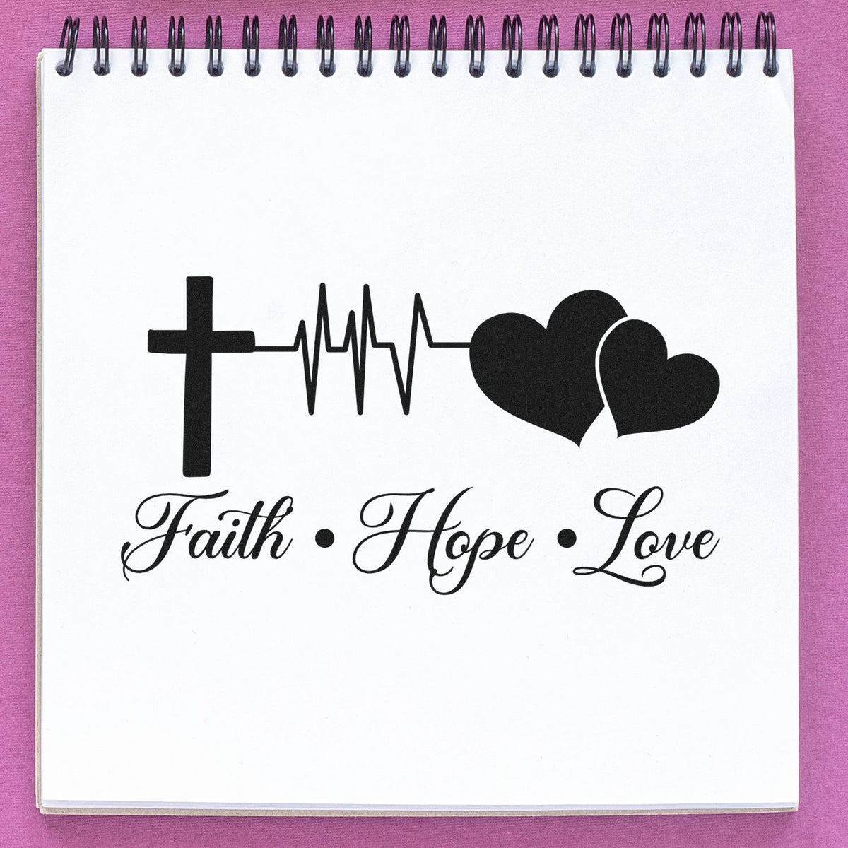 Black faith, hope, love stamp and seal design with cross, heartbeat line, and hearts on a white spiral notebook against a pink background.
