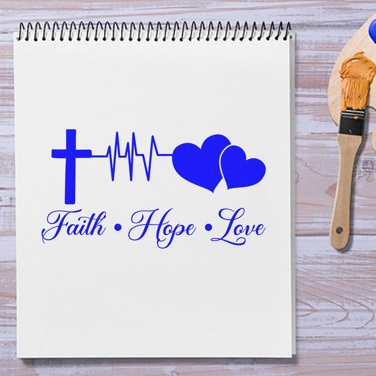 Blue faith hope love stamp and seal design with cross, heartbeat line and hearts on white page; wood-handled brush seal nearby