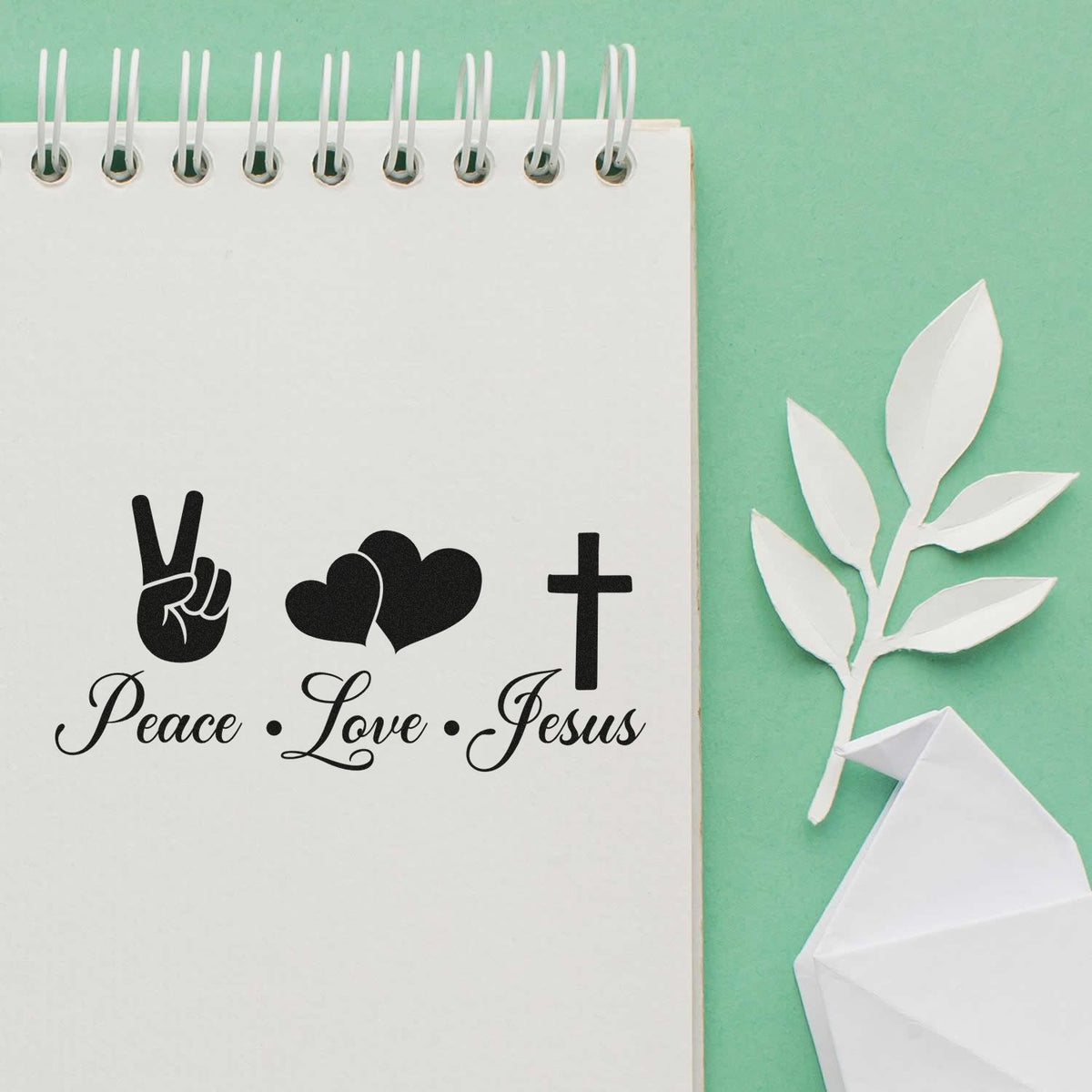 Black Peace Love Jesus stamp and seal design with peace sign, hearts and cross on white spiral notebook, mint green background.