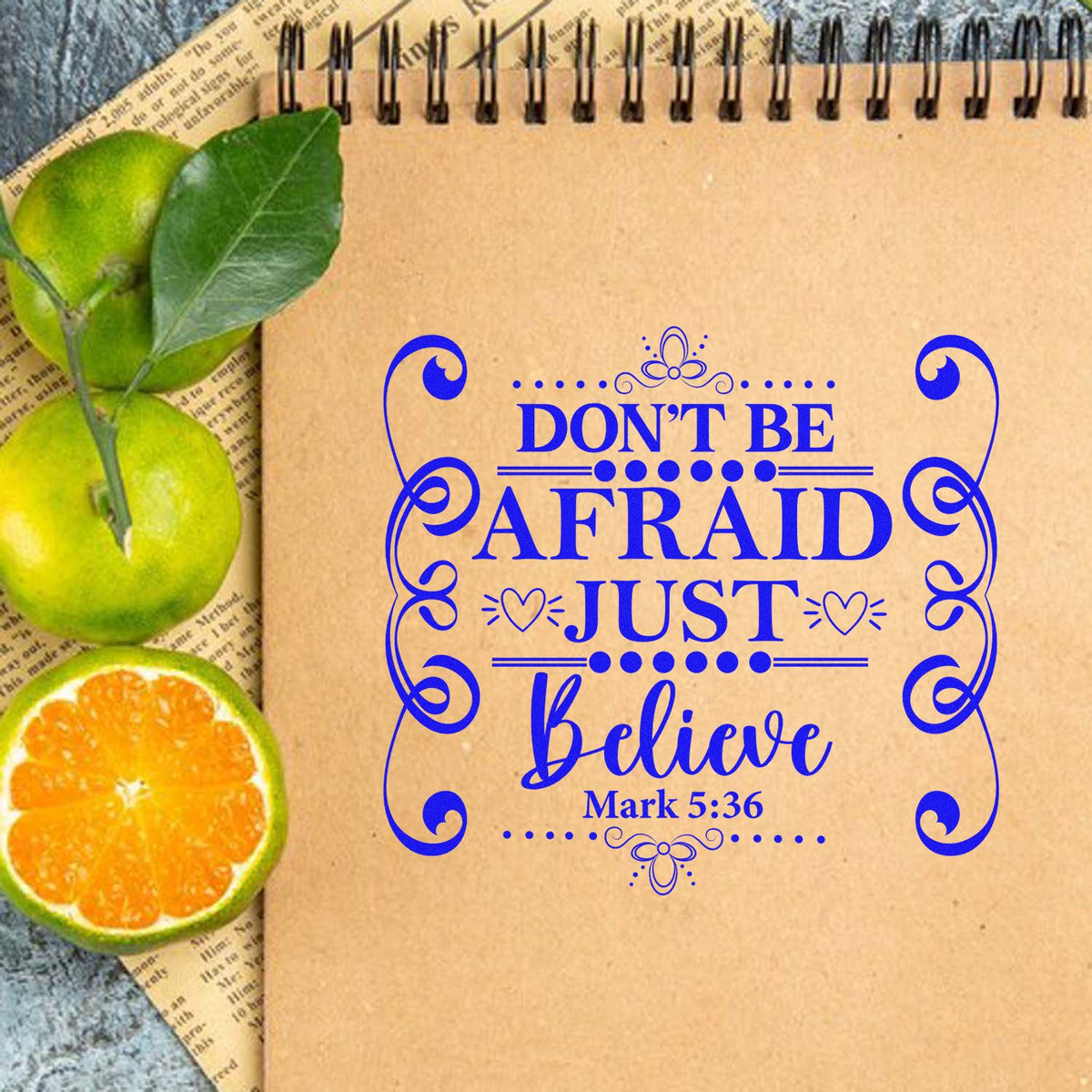 Blue decorative stamp and seal reading Dont be afraid, just believe on kraft notebook with green citrus slices.