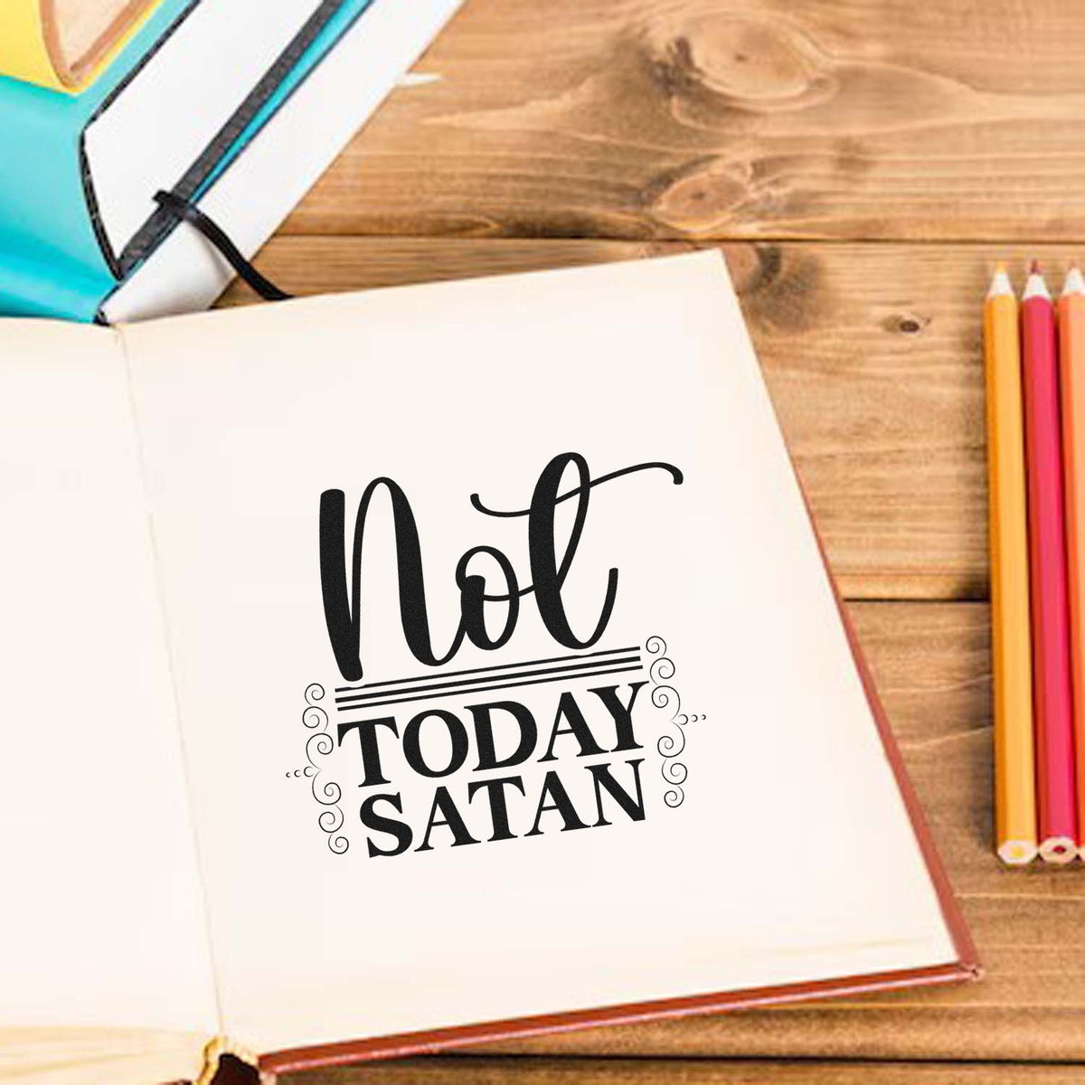Black Not Today Satan stamp and seal on open notebook, with teal, yellow, pink, and orange pencils on a wooden desk.