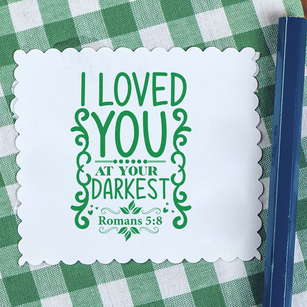 Green religious stamp seal on white scalloped card, reading I Loved You at Your Darkest and Romans 5:8, on green gingham.