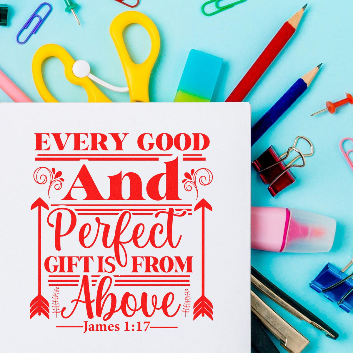 White card with red scripture stamp, surrounded by colorful stamp and seal supplies, pencils and clips on turquoise background.