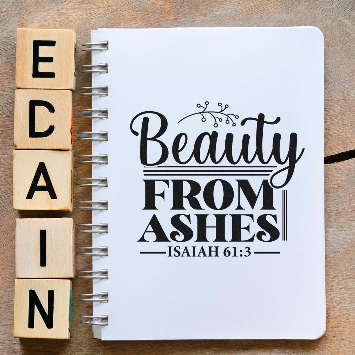 Wooden alphabet stamp blocks beside a white spiral notebook with black Beauty from Ashes seal design and Isaiah 61:3.
