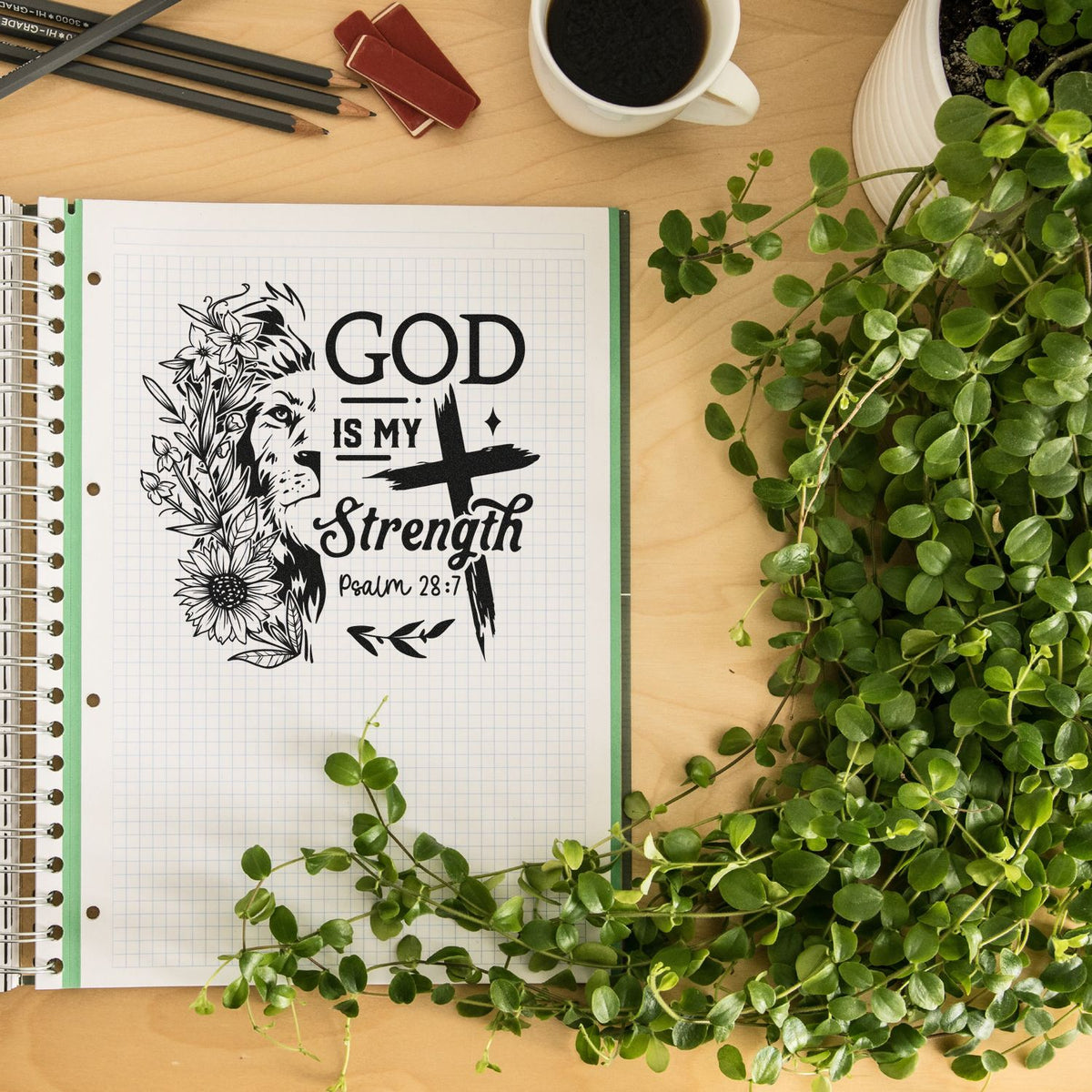 Black faith rubber stamp design on grid notebook page: lion, flowers, and God Is My Strength, Psalm 28:7, with green leaves.