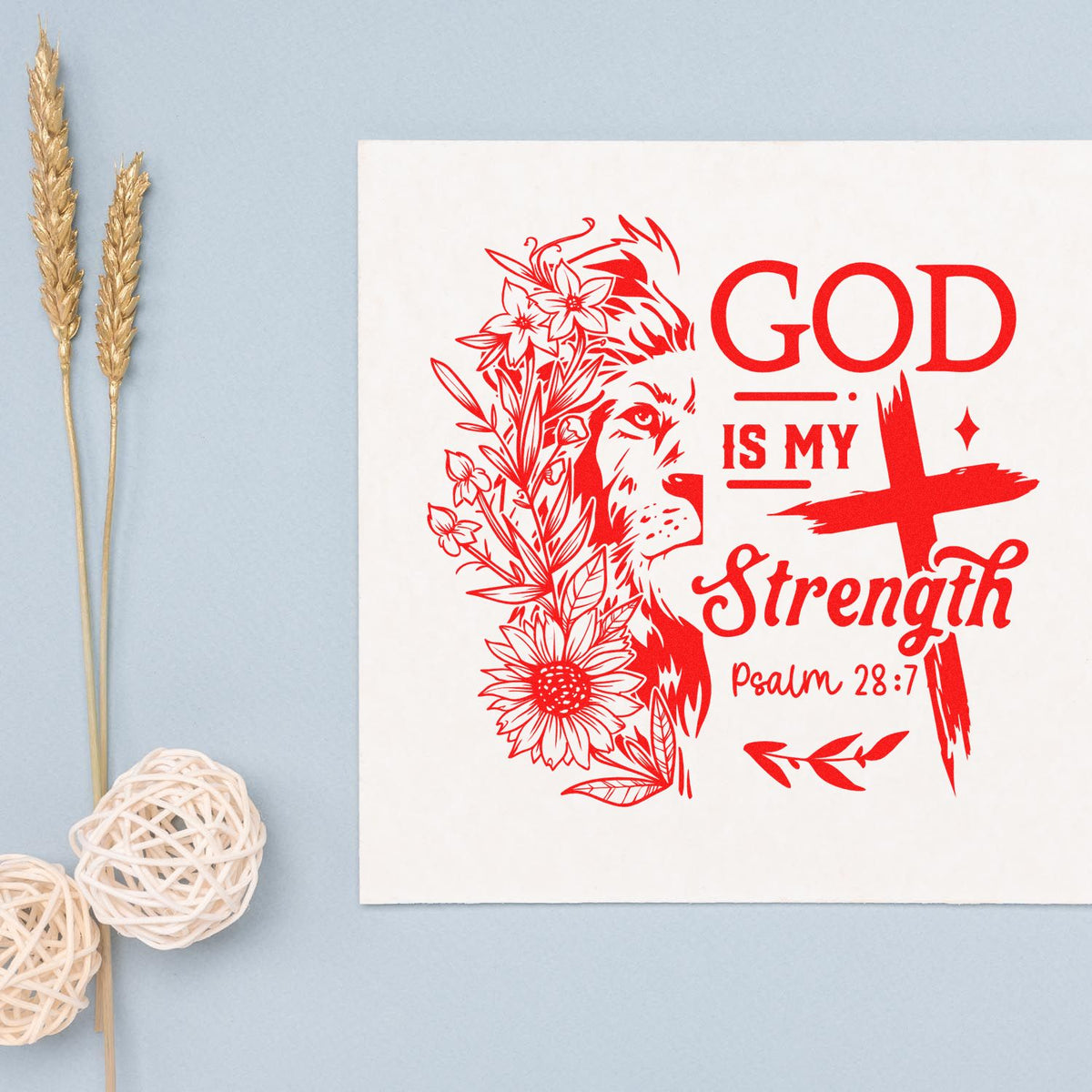 Red custom stamp seal design with lion, floral cross, and Psalm 28:7 on a white card, beside dried wheat and woven decor.