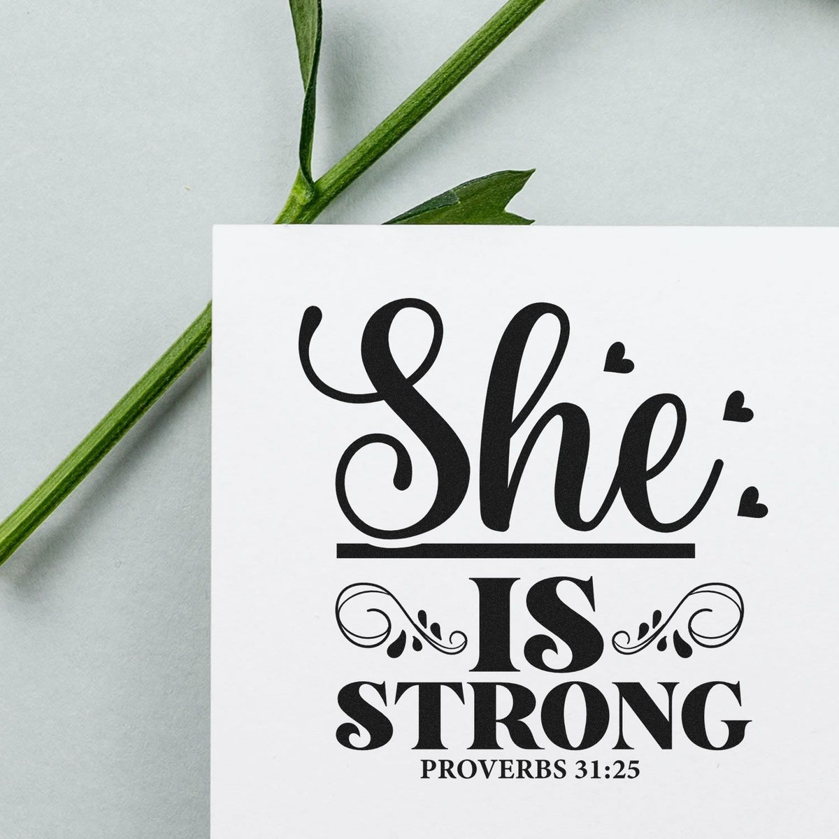 Black She is strong Proverbs 31:25 stamp and seal on white card with decorative hearts and green leaves.