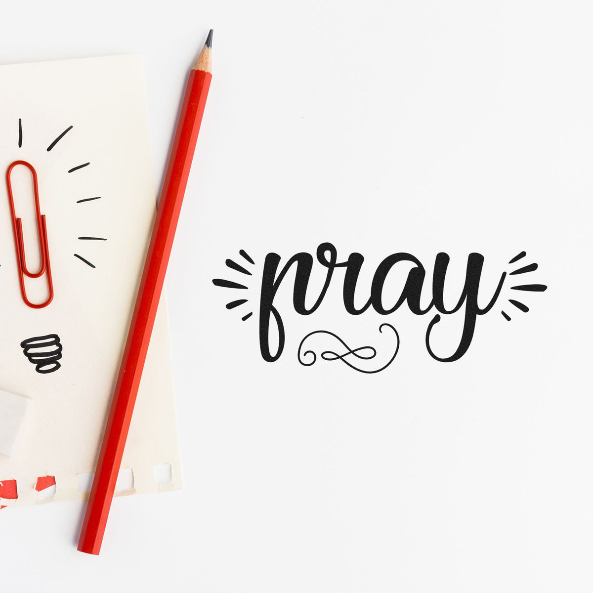 Red pencil and paper clip beside a black pray decorative stamp and seal on white stationery.