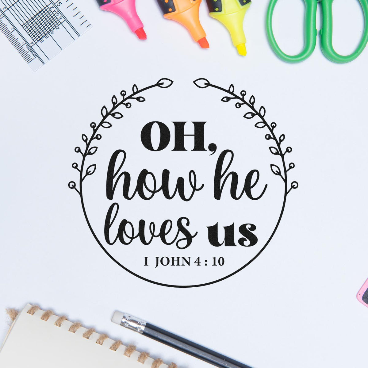 Black custom stamp and seal design reading Oh, how he loves us, framed by a leafy wreath, with colorful markers and tools around it.