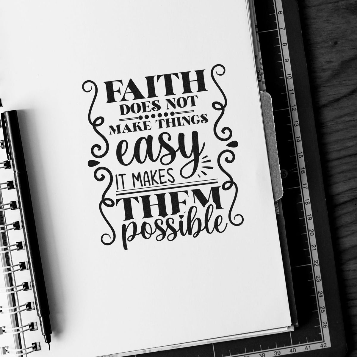 Black decorative faith quote stamp/seal on white paper, with swirl accents in a spiral notebook.
