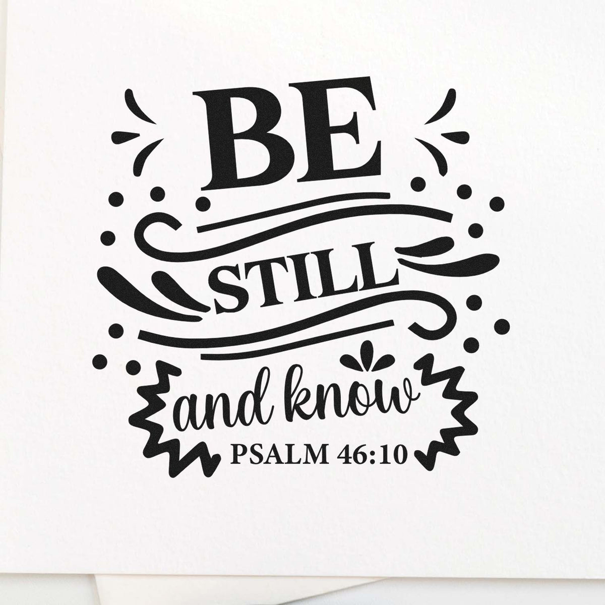 Black decorative stamp and seal reading BE STILL and know with Psalm 46:10 on a white background.