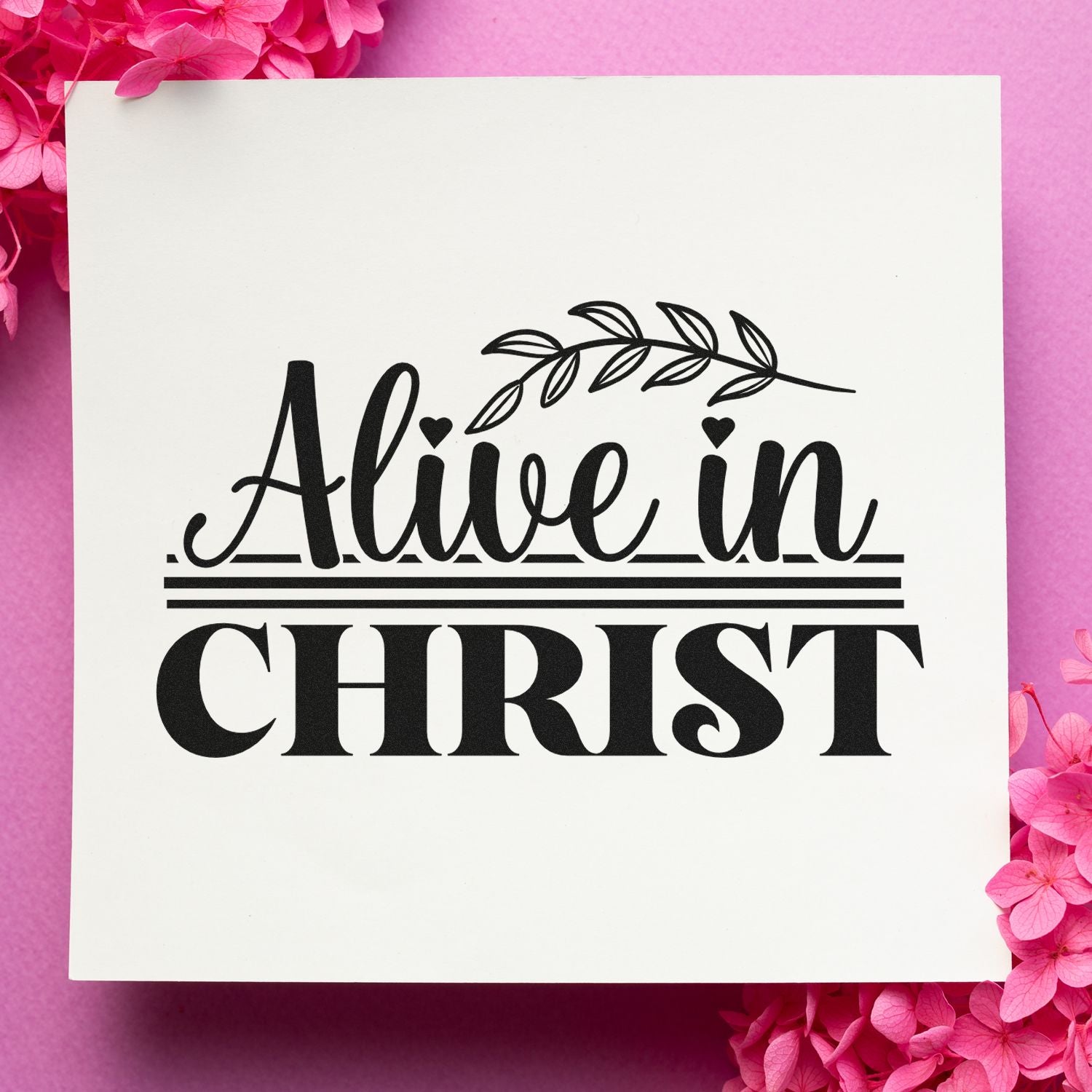 Black "Alive in Christ" stamp seal with leaf branch on white background, framed by pink flowers.