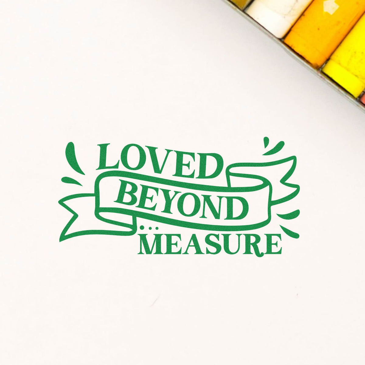 Green Loved Beyond Measure ribbon stamp and seal design on white, with colorful packaging corner.