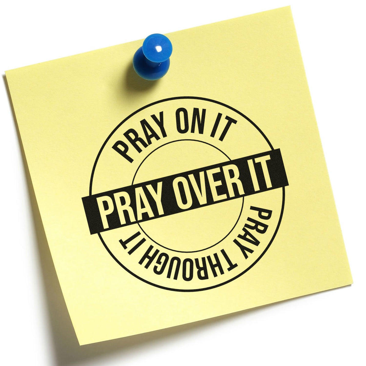 Yellow sticky note with blue pushpin and black circular rubber stamp seal reading Pray on it, pray over it, pray through it.