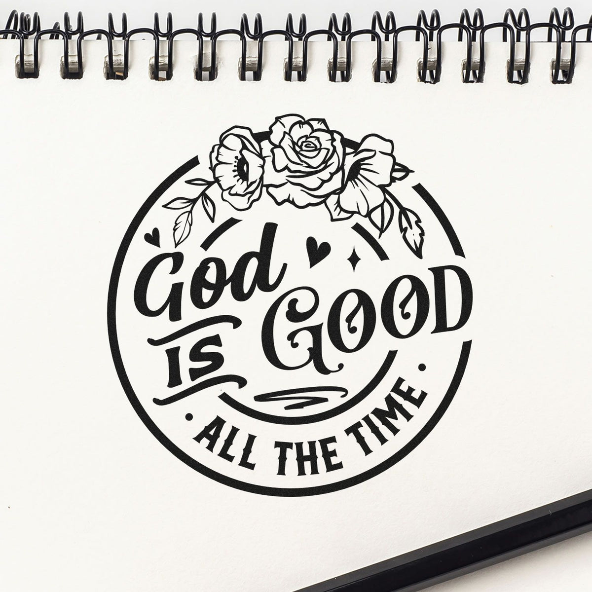 Black floral stamp seal reading God is Good All the Time on a white spiral notebook page.