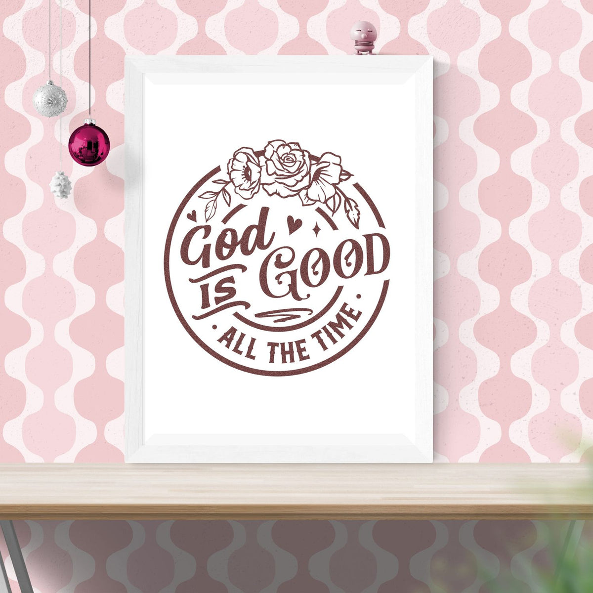 Brown floral stamp and seal design reading God Is Good All the Time in dark brown on white, framed against a pink patterned wall.