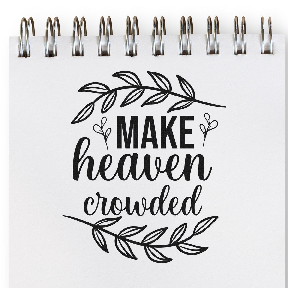 Black botanical stamp/seal design on white spiral notebook with Make heaven crowded script and leafy wreath.