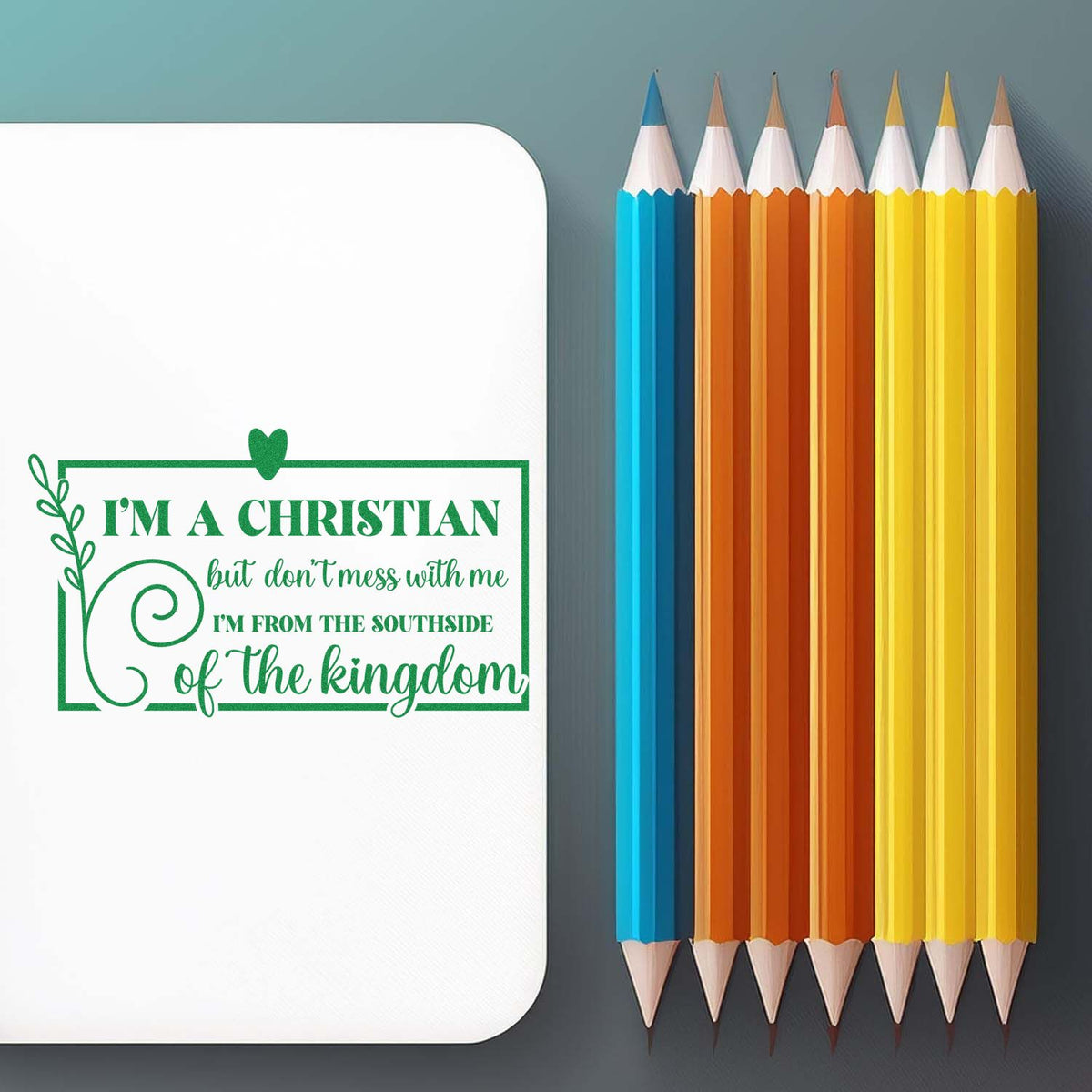 Green Christian stamp seal on white card beside blue, orange, and yellow pencils against a gray background.