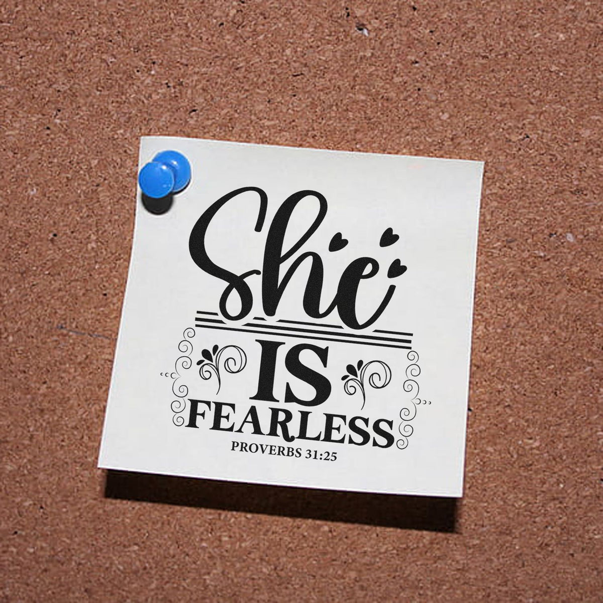 White stamp and seal sample pinned with blue tacks, featuring black She is Fearless text and Proverbs 31:25 on cork board.