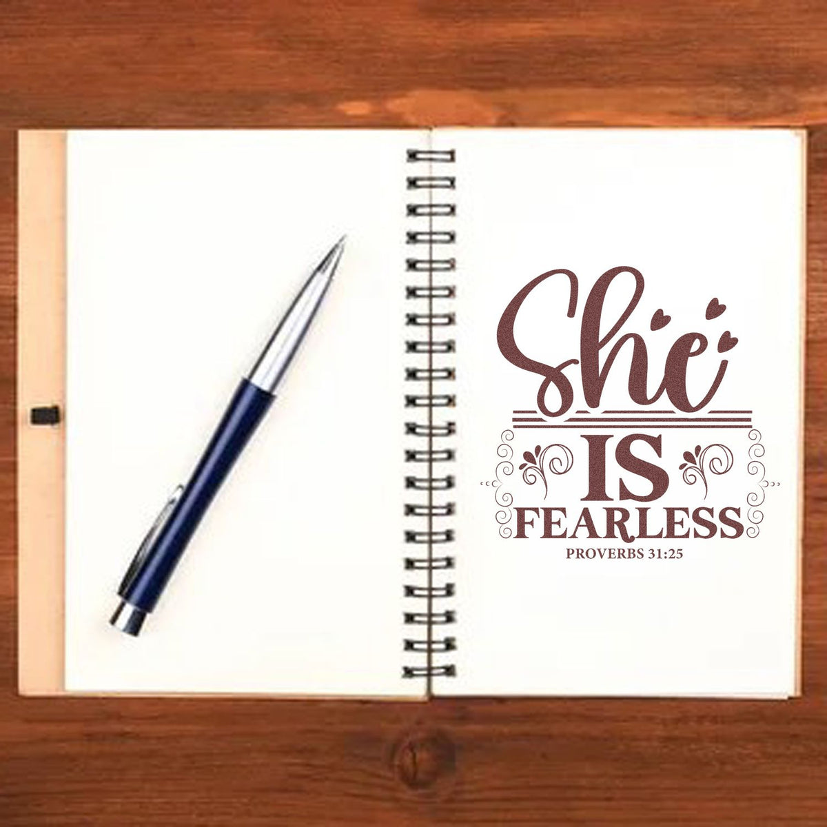 Custom brown maroon stamp and seal reading She Is Fearless on a spiral notebook, with a blue pen on white pages.