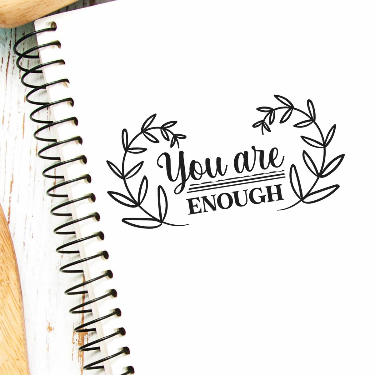 Black You are Enough stamp seal with leafy wreath on a white spiral notebook