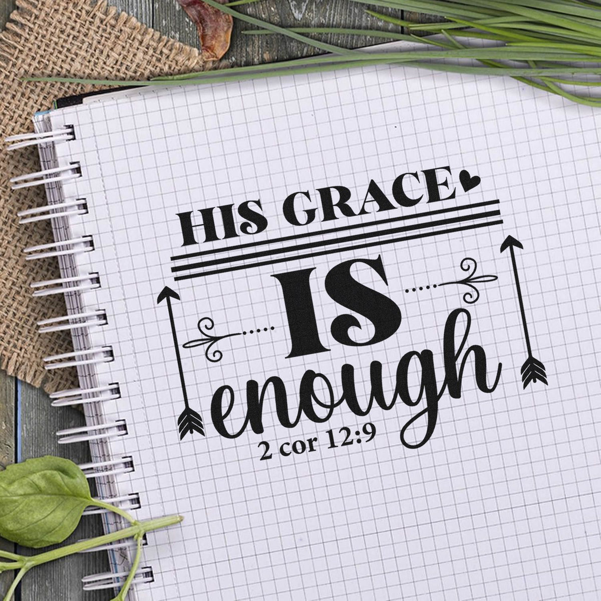 Black stamp and seal design on white grid paper reading His Grace is enough with arrows, heart, and 2 Cor 12:9.
