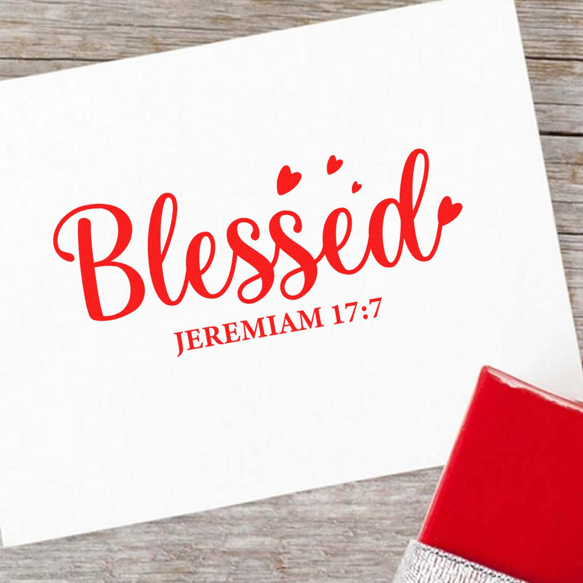 Red Blessed Jeremiah 17:7 stamp and seal design on white paper with hearts, plus a red stamp pad on wood.