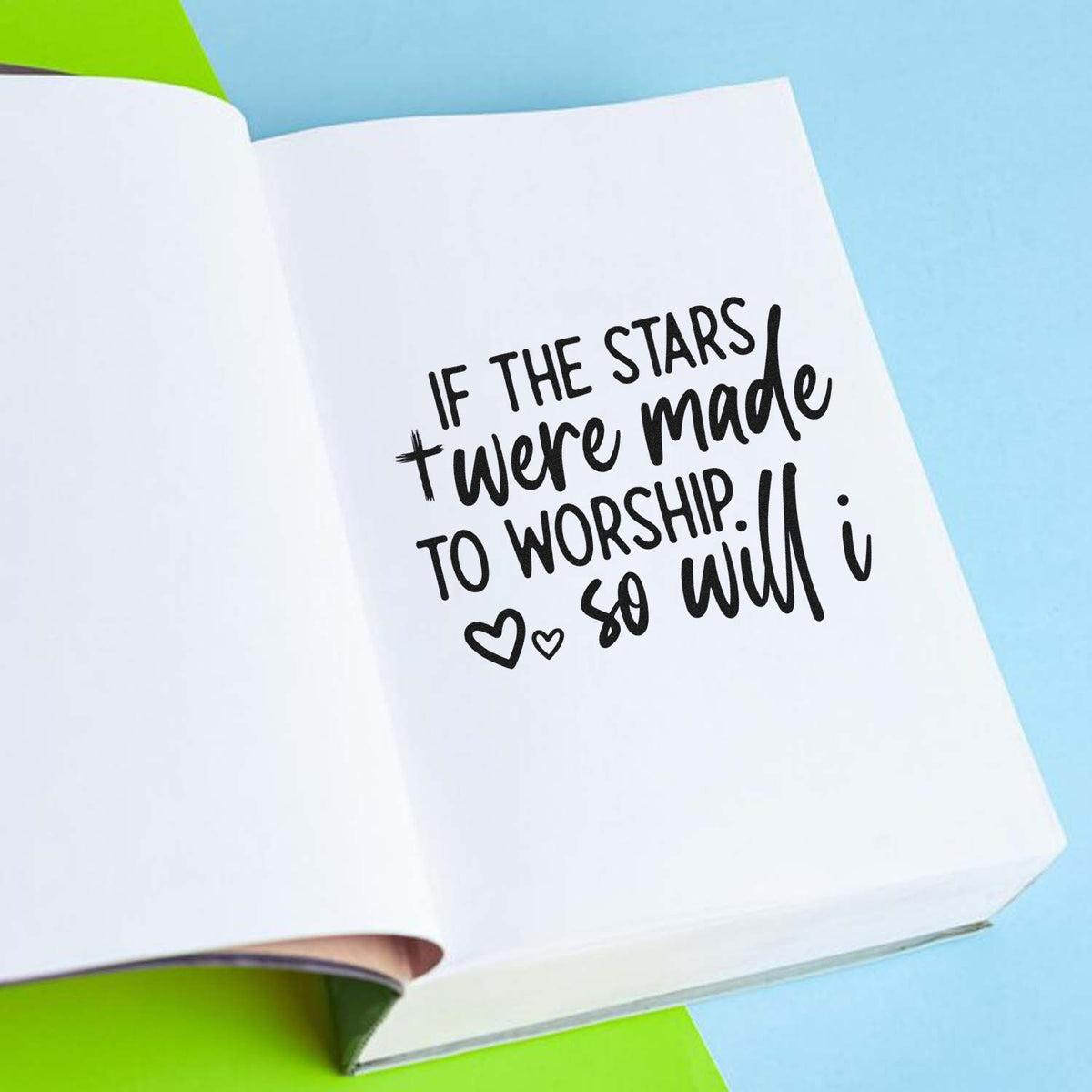 Black rubber stamp/seal-style quote with hearts on white notebook pages, over blue and lime background.