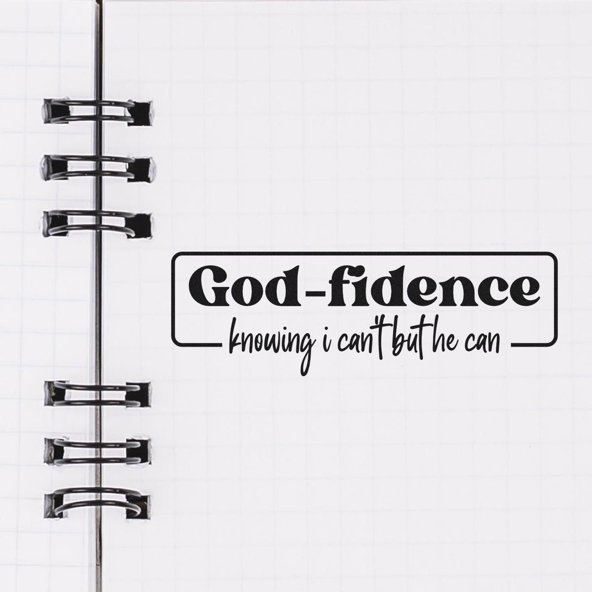Black God-fidence stamp seal on white grid notebook page with spiral binding.
