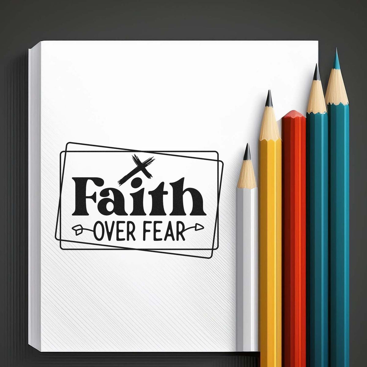 Black Faith over Fear stamp and seal design on a white notebook, beside colorful pencils.
